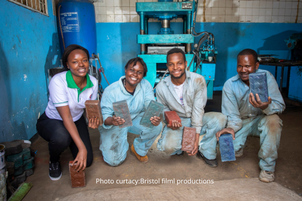 Werknemers van Gjenge Makers poseren met duurzame bakstenen gemaakt van plastic afval.